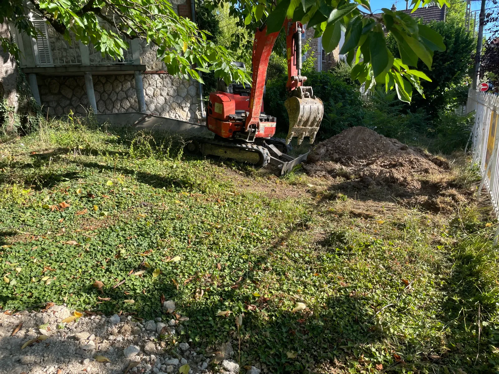 Mini-pelle en cours de terrassement dans un jardin devant une maison en meulière, en Essonne