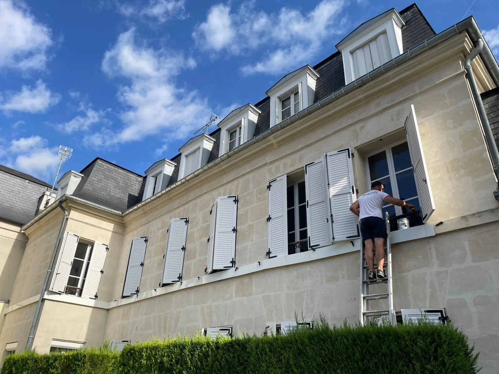Façade en pierre de taille d'une grande demeure en cours de ravalement, un compagnon travaille depuis une échelle