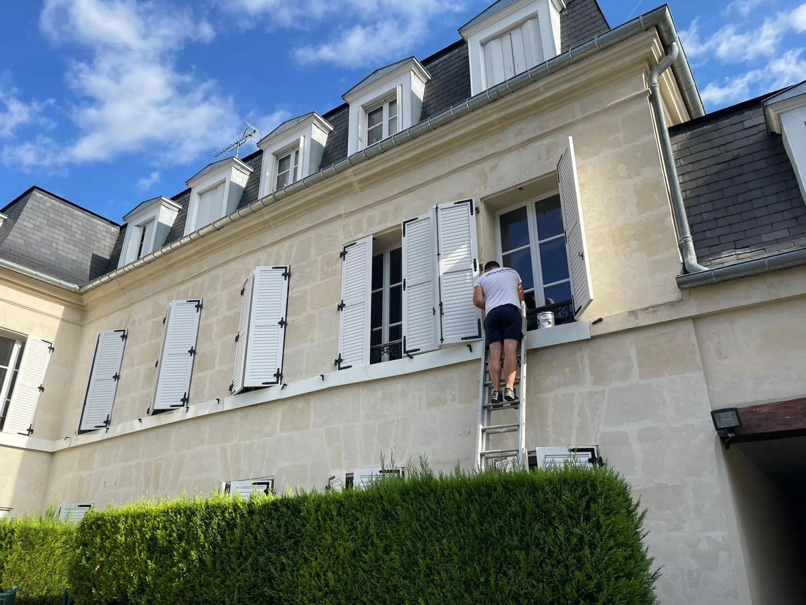Grande demeure en pierre de taille aux volets blancs, façade ravalée sous un ciel dégagé