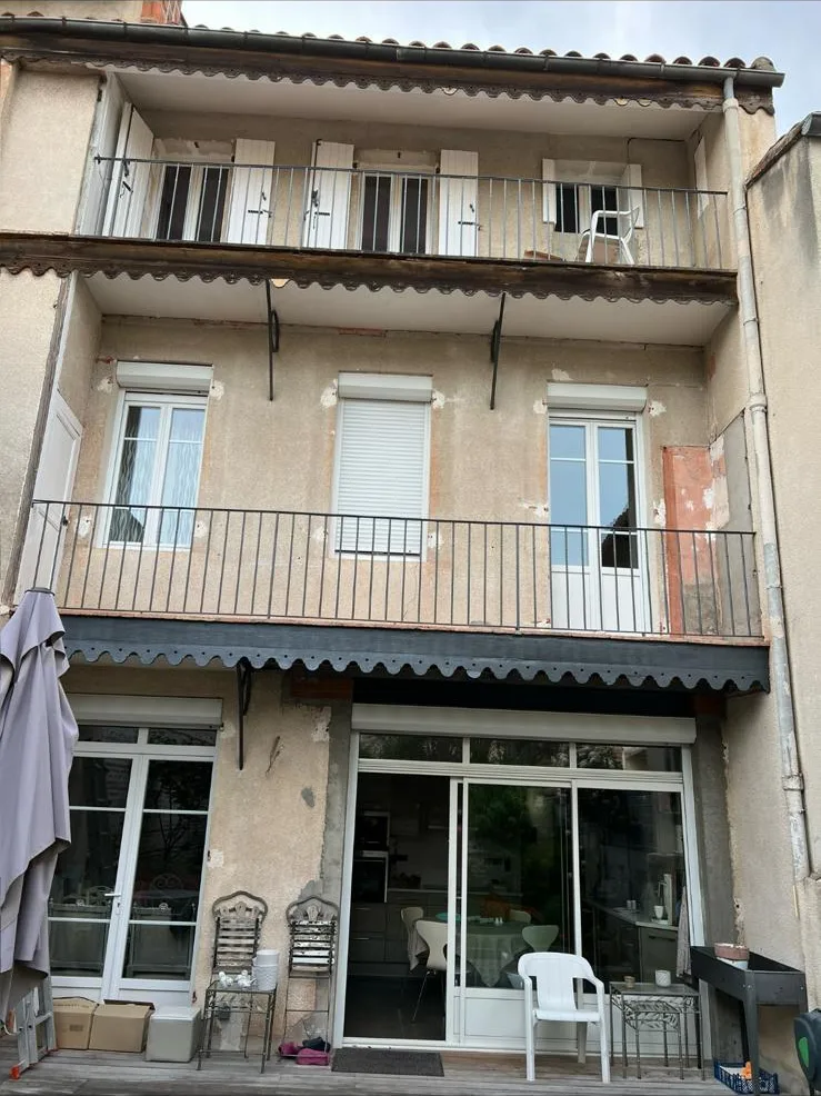 Façade de maison de ville avant ravalement : crépi gris terni, taches et reprises rougeâtres, enduit cloqué autour des balcons