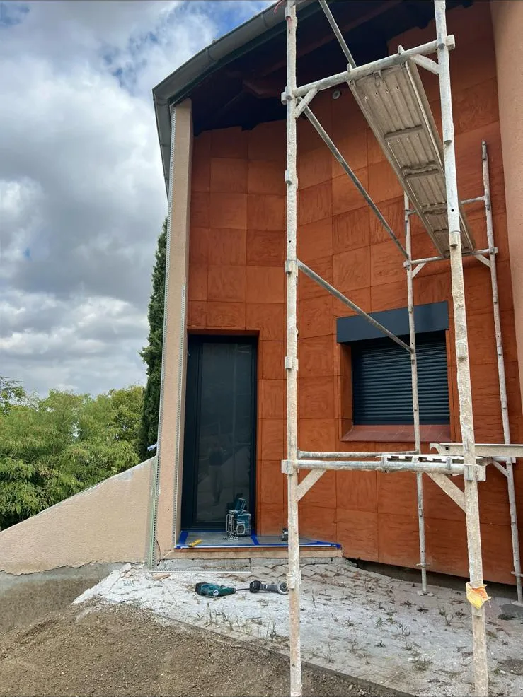 Angle de villa recouvert d'un enduit ocre terracotta fraîchement projeté, échafaudage en place