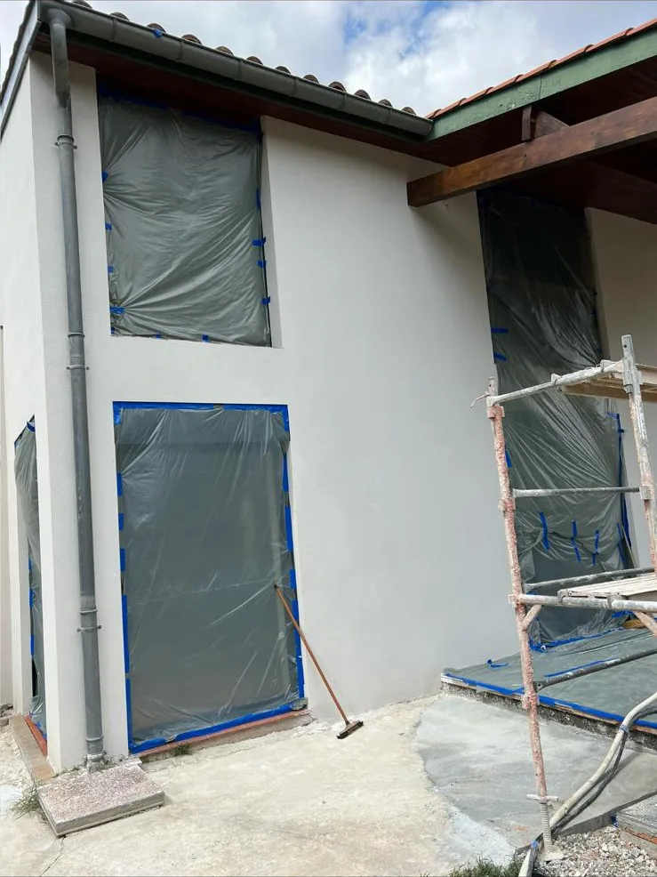 Maison à l'enduit blanc terminé, ouvertures entièrement protégées par un film et du ruban de masquage, échafaudage en place